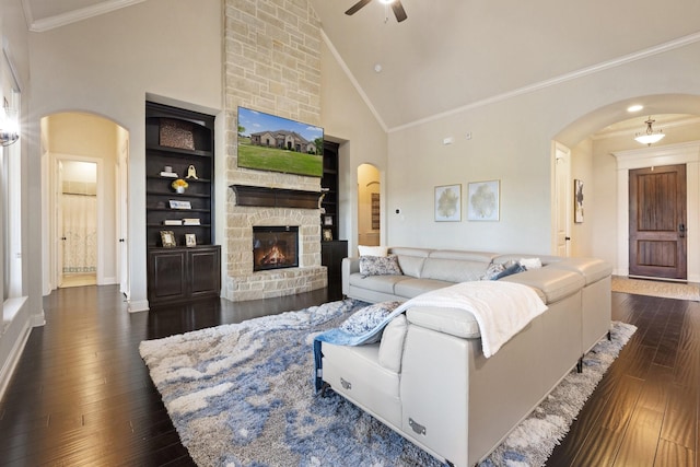 living room featuring a fireplace, a ceiling fan, crown molding, dark wood finished floors, and arched walkways