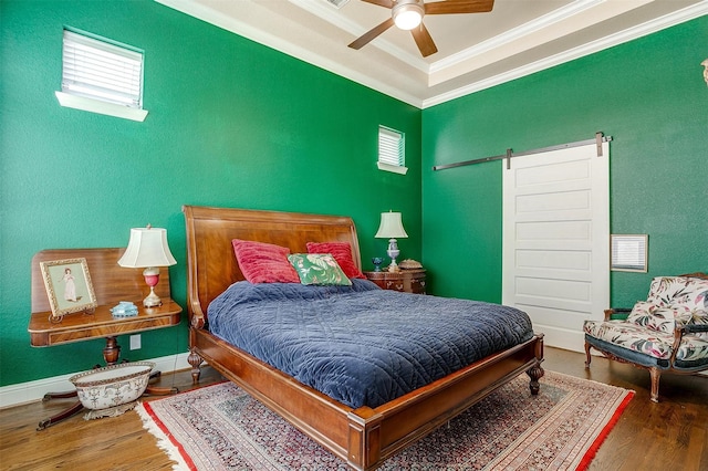 bedroom with crown molding, wood finished floors, ceiling fan, and a barn door