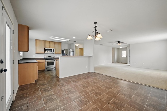 kitchen featuring dark countertops, open floor plan, ceiling fan with notable chandelier, hanging light fixtures, and stainless steel appliances