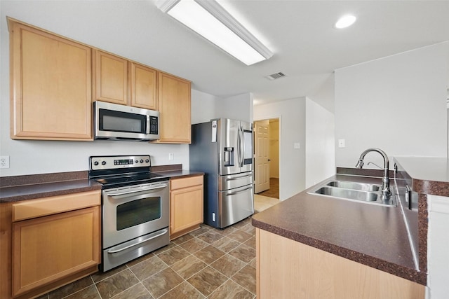 kitchen with dark countertops, a sink, light brown cabinets, stainless steel appliances, and visible vents