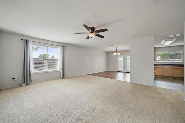 unfurnished living room featuring carpet floors, baseboards, ceiling fan with notable chandelier, and visible vents