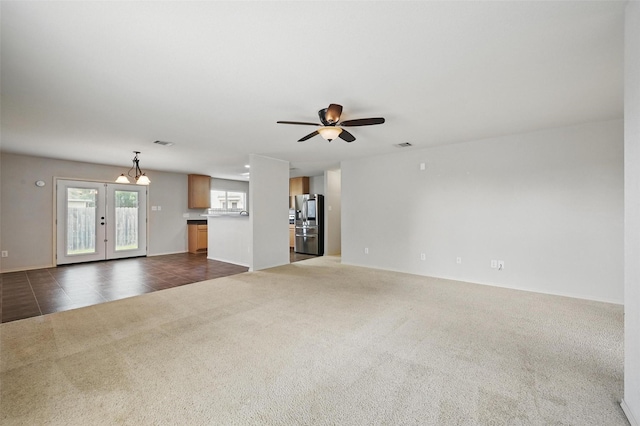 unfurnished living room featuring french doors, ceiling fan with notable chandelier, dark colored carpet, baseboards, and visible vents