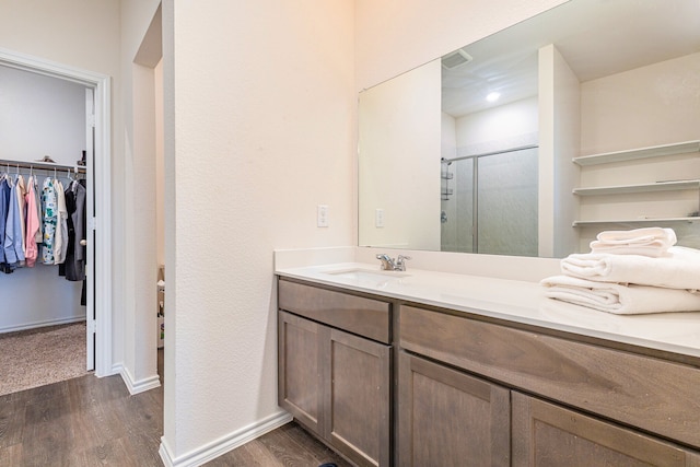 bathroom featuring a shower stall, a walk in closet, vanity, and wood finished floors