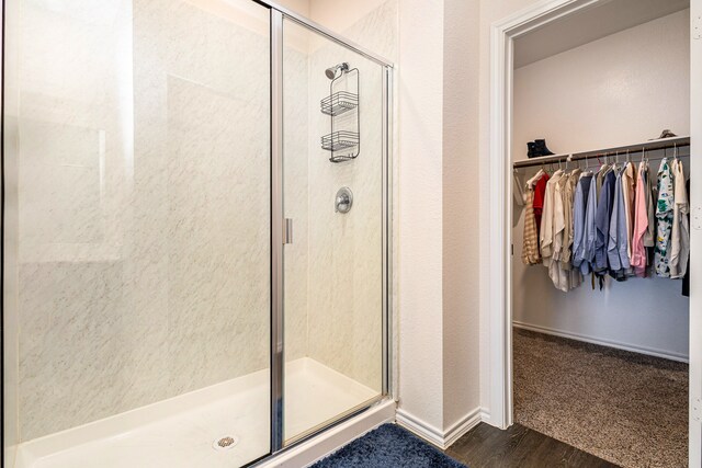 bathroom featuring wood finished floors, baseboards, a spacious closet, and a shower stall