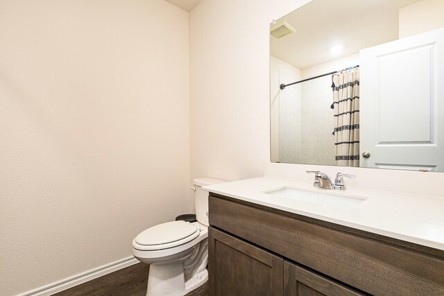 bathroom with wood finished floors, vanity, baseboards, toilet, and visible vents