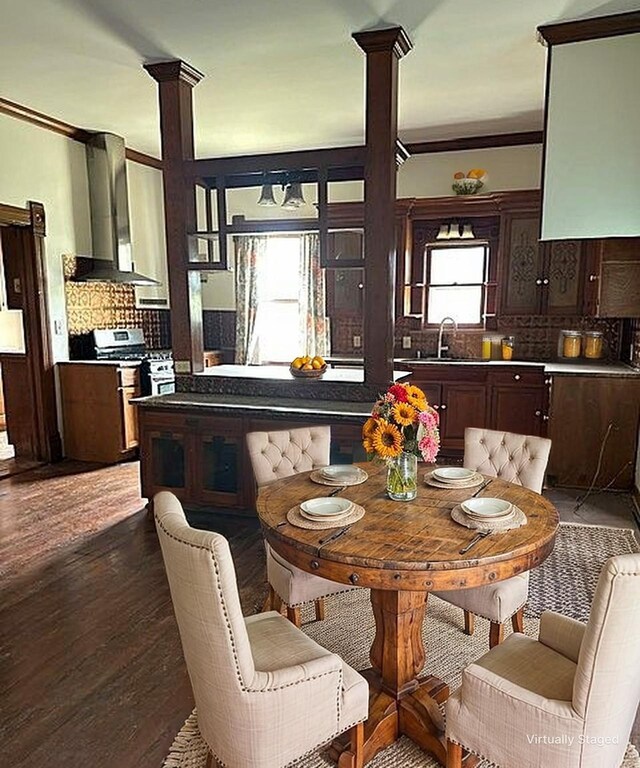 kitchen with wall chimney exhaust hood, a sink, stainless steel gas range, tasteful backsplash, and decorative columns