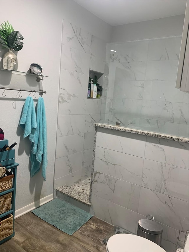 bathroom featuring toilet, baseboards, wood finished floors, and walk in shower