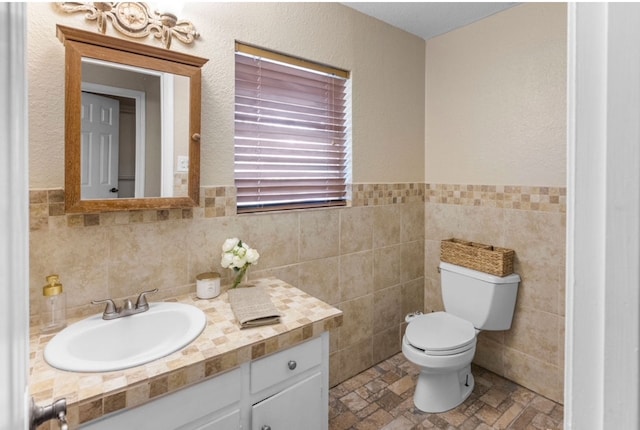 800 Western Hills Dr, Sherman, TX 75092 - half bathroom featuring vanity, a wainscoted wall, toilet, stone finish flooring, and tile walls
