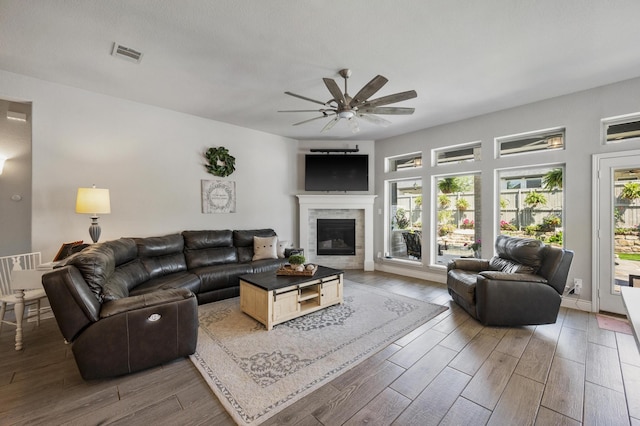 living area featuring wood finished floors, ceiling fan, a glass covered fireplace, and visible vents