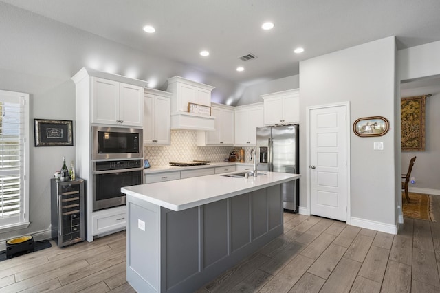 kitchen with light wood-type flooring, visible vents, appliances with stainless steel finishes, a sink, and beverage cooler