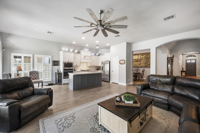 living area with arched walkways, visible vents, light wood-type flooring, and a ceiling fan