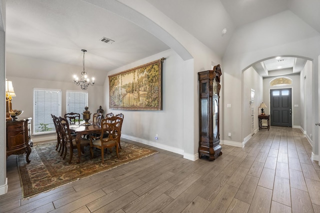 dining space featuring baseboards, a chandelier, visible vents, arched walkways, and wood finished floors