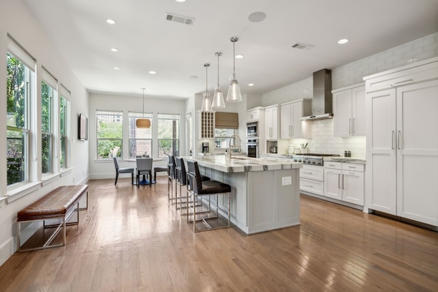 3912 Holland Ave, Dallas, TX 75219 - kitchen featuring wall chimney exhaust hood, stainless steel appliances, white cabinets, wood finished floors, and recessed lighting