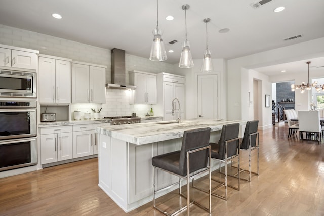3912 Holland Ave, Dallas, TX 75219 - kitchen with stainless steel appliances, wall chimney range hood, a sink, decorative backsplash, and a chandelier