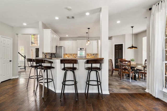 5800 Edgewood Dr, Mckinney, TX 75072 - kitchen featuring decorative backsplash, a breakfast bar, a peninsula, appliances with stainless steel finishes, and dark wood-style floors