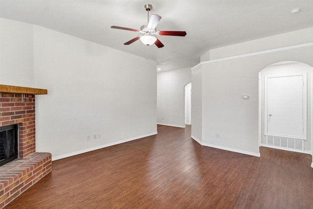 unfurnished living room featuring arched walkways, wood finished floors, a fireplace, and a ceiling fan