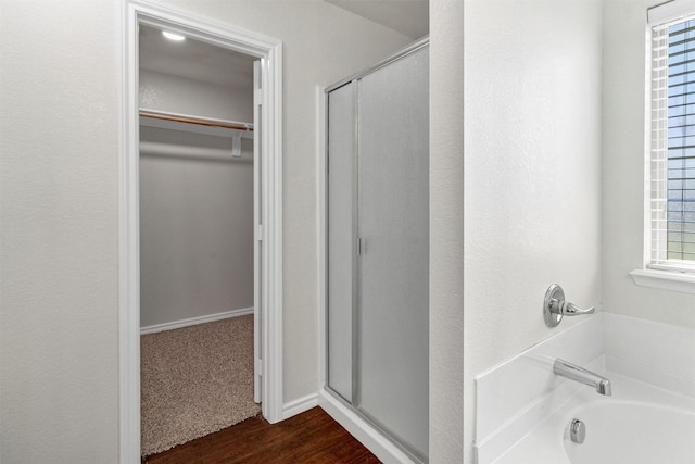 bathroom featuring a shower stall, a garden tub, wood finished floors, and a spacious closet