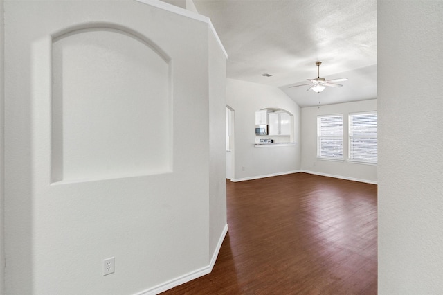 interior space featuring baseboards, arched walkways, a ceiling fan, dark wood finished floors, and vaulted ceiling