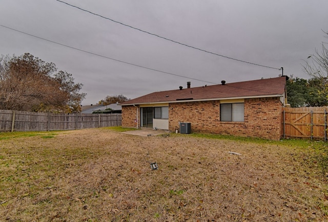 rear view of house with a yard, brick siding, central air condition unit, and a fenced backyard