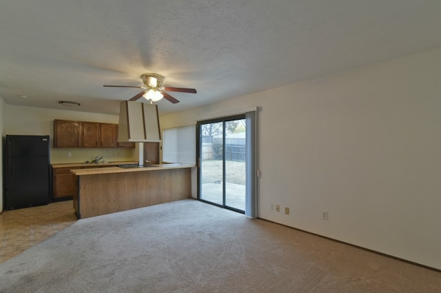 kitchen featuring freestanding refrigerator, a peninsula, a ceiling fan, light carpet, and light countertops