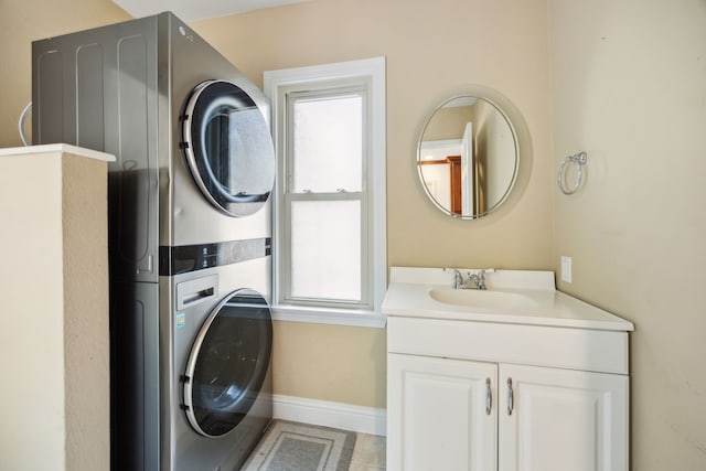 laundry area featuring stacked washer and clothes dryer, a healthy amount of sunlight, baseboards, and a sink