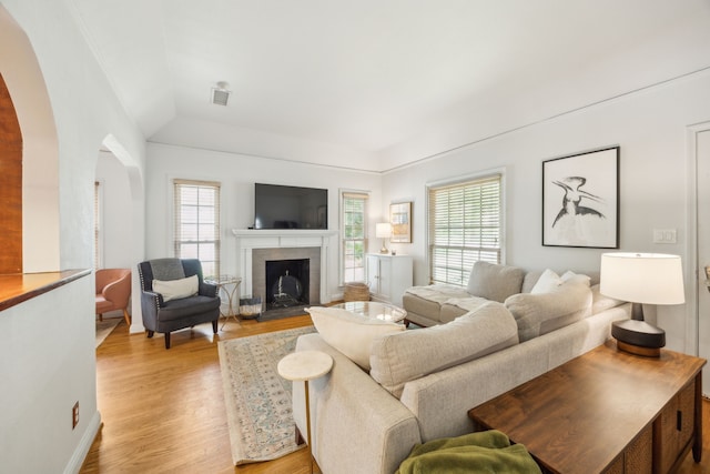 living area with a fireplace, arched walkways, visible vents, and light wood-type flooring