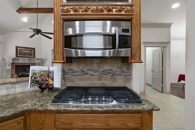 kitchen with appliances with stainless steel finishes, a fireplace, brown cabinetry, a ceiling fan, and tasteful backsplash