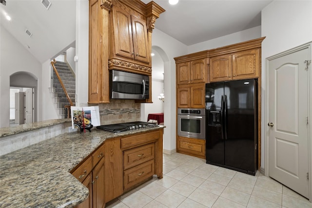 kitchen featuring appliances with stainless steel finishes, tasteful backsplash, arched walkways, and dark stone countertops