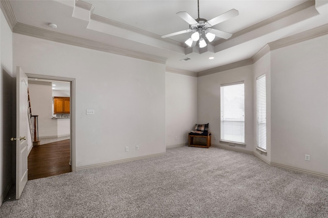 carpeted spare room with crown molding, a ceiling fan, baseboards, a tray ceiling, and visible vents