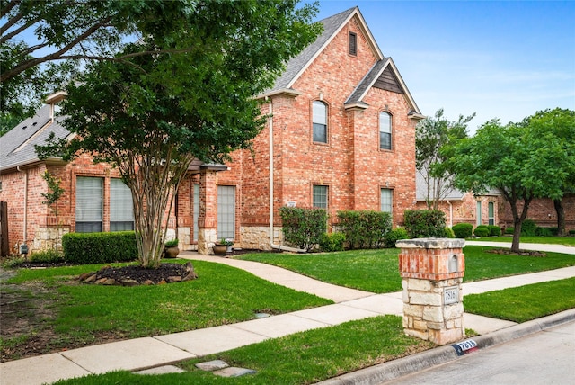 view of front facade featuring a shingled roof, a front lawn, and brick siding