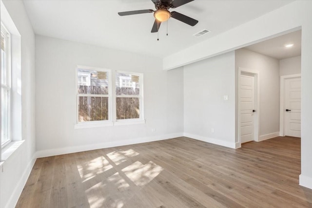 empty room with visible vents, ceiling fan, plenty of natural light, and wood finished floors