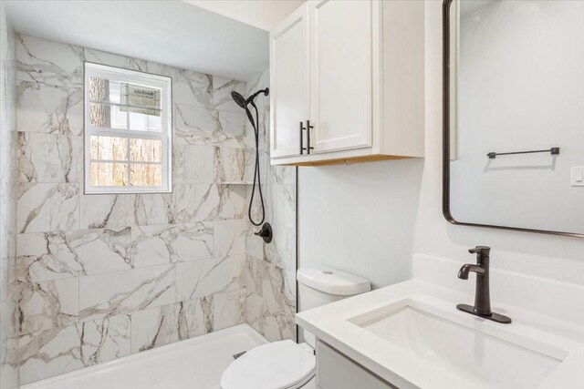 full bathroom featuring a tile shower, vanity, and toilet