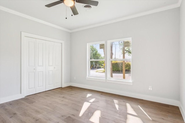 unfurnished bedroom featuring a closet, ornamental molding, visible vents, wood finished floors, and baseboards