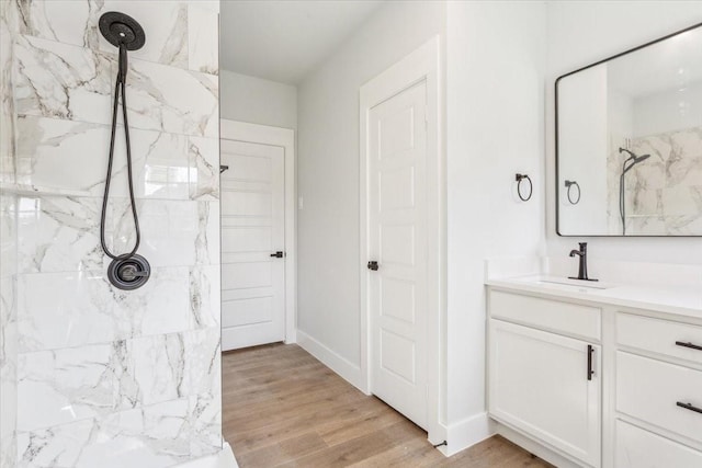 full bath featuring wood finished floors, a marble finish shower, baseboards, and vanity