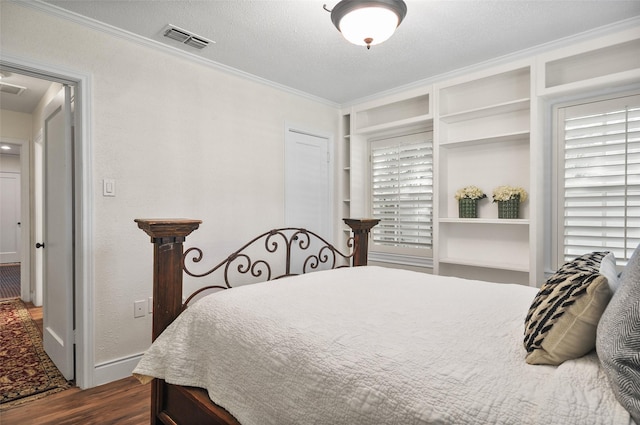 bedroom with a textured ceiling, ornamental molding, dark wood finished floors, and visible vents
