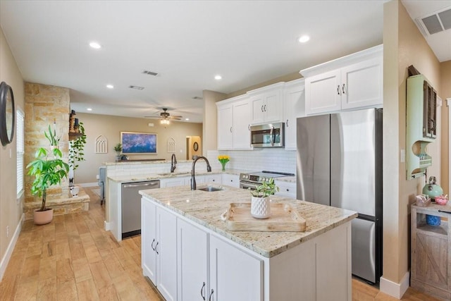 kitchen with visible vents, a sink, a peninsula, stainless steel appliances, and an island with sink
