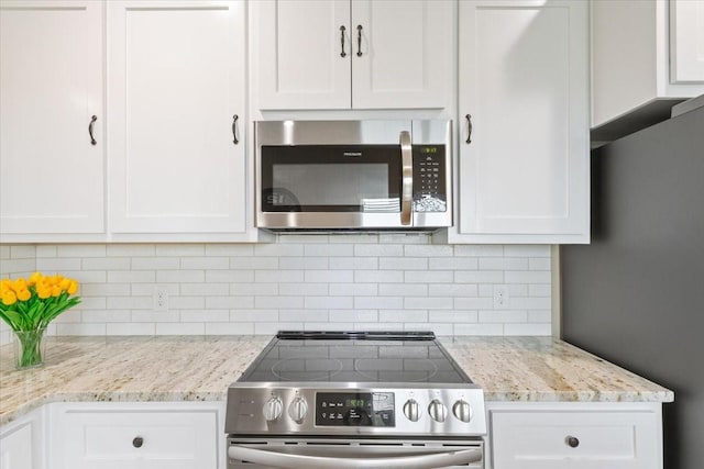 kitchen with appliances with stainless steel finishes, light stone countertops, backsplash, and white cabinetry