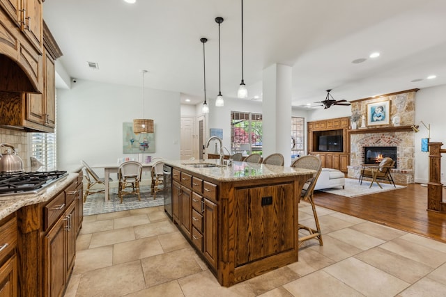 kitchen with a kitchen breakfast bar, a stone fireplace, a ceiling fan, a sink, and appliances with stainless steel finishes