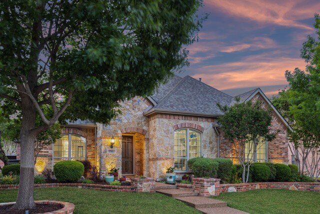 french country inspired facade featuring brick siding, stone siding, a front yard, and a shingled roof