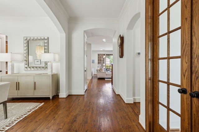 corridor featuring baseboards, dark wood-style floors, arched walkways, and crown molding