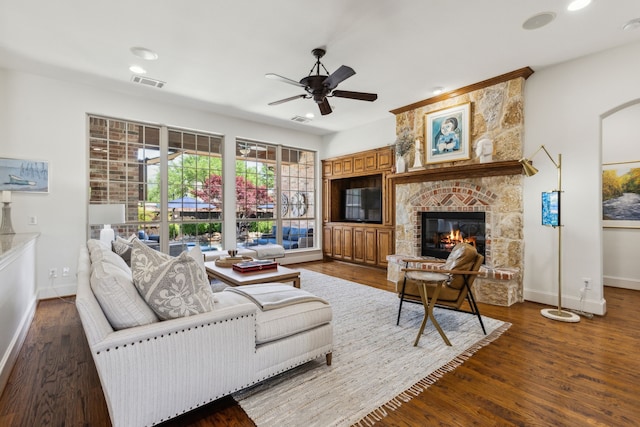 living room with baseboards, a stone fireplace, visible vents, and ceiling fan