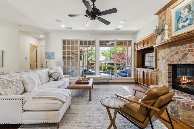 living room featuring a brick fireplace, wood finished floors, visible vents, and a ceiling fan