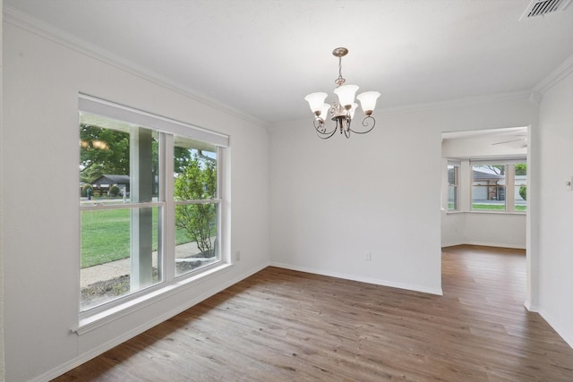 spare room with an inviting chandelier, ornamental molding, visible vents, wood finished floors, and baseboards