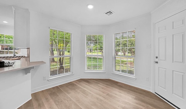 unfurnished dining area featuring baseboards, a sink, visible vents, and light wood-style flooring