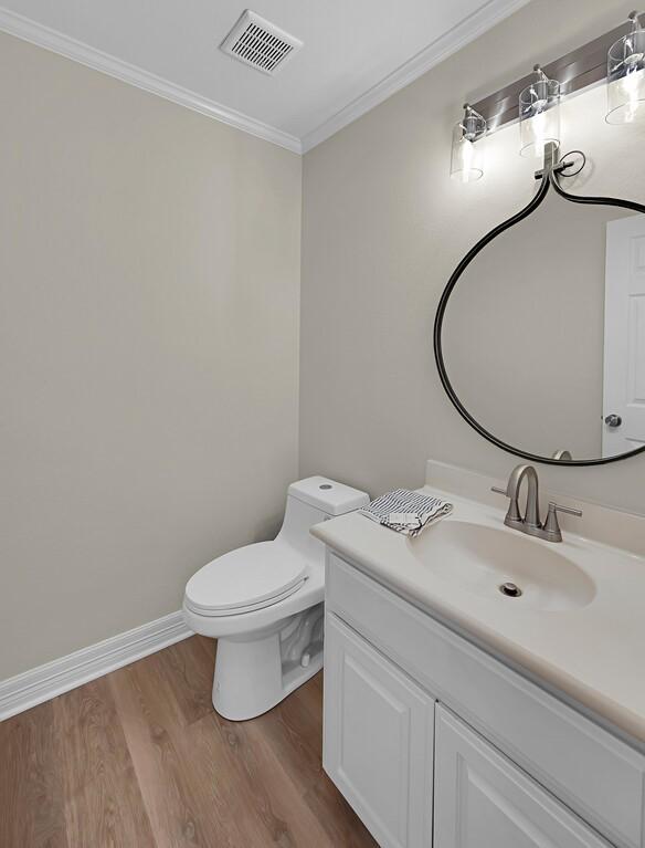 half bath with wood finished floors, vanity, toilet, ornamental molding, and visible vents
