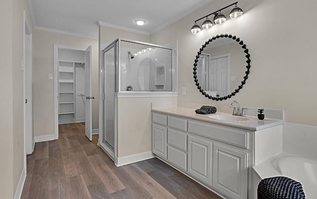 bathroom featuring wood finished floors, a shower stall, a walk in closet, vanity, and ornamental molding