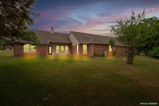 back of property featuring a chimney, roof with shingles, brick siding, and a yard