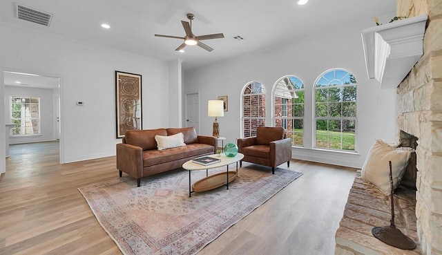 living room featuring light wood-style floors, a stone fireplace, visible vents, and ceiling fan