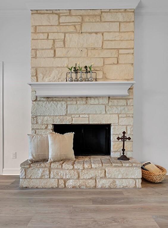 room details featuring wood finished floors, a stone fireplace, and crown molding