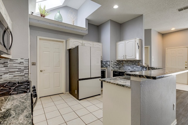 kitchen featuring stainless steel microwave, visible vents, freestanding refrigerator, a peninsula, and backsplash